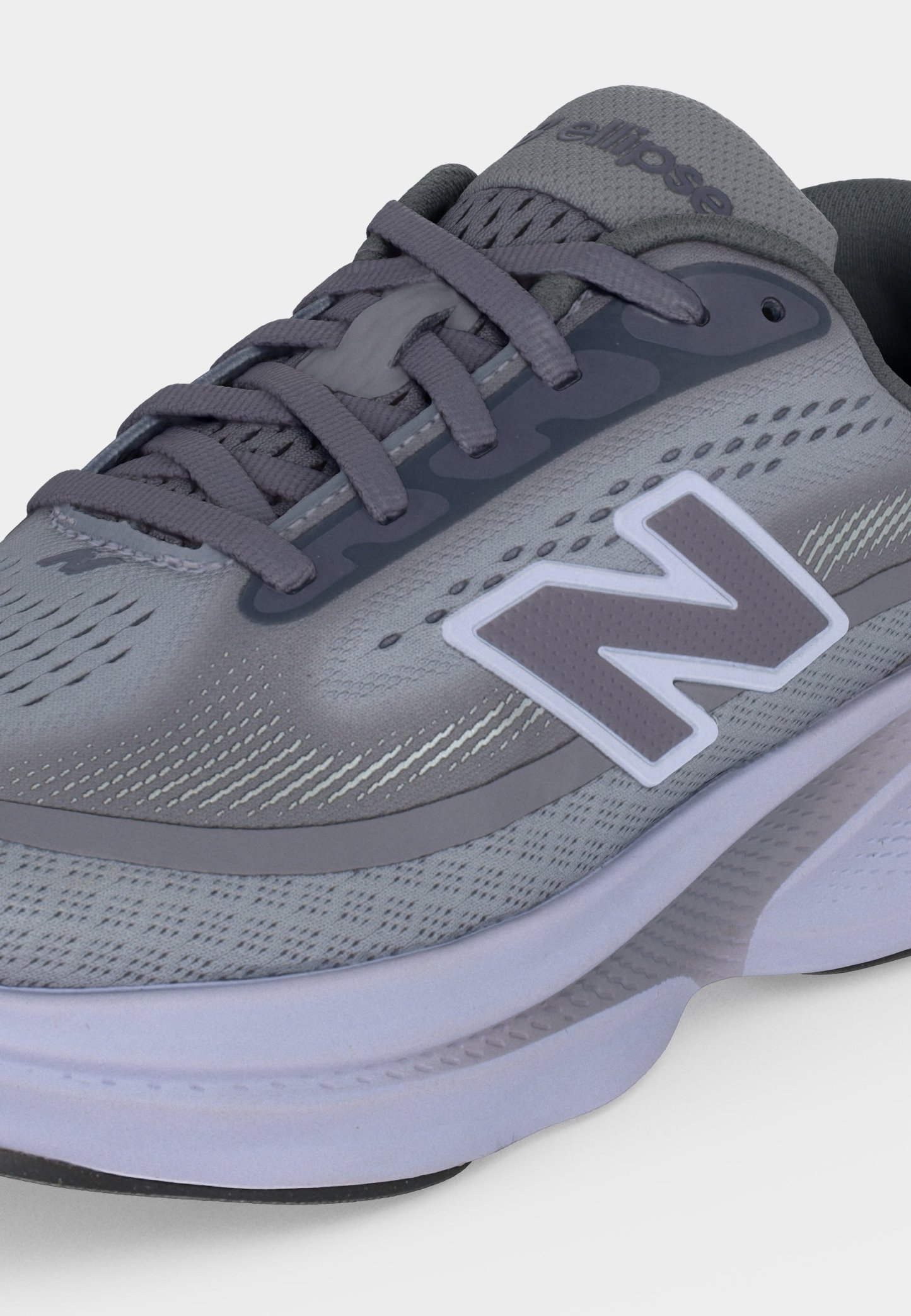 Zapatilla deportiva New Balance gris con suela blanca, parte superior de malla y cordones grises, con un gran logo "N" blanco y gris en el lado.