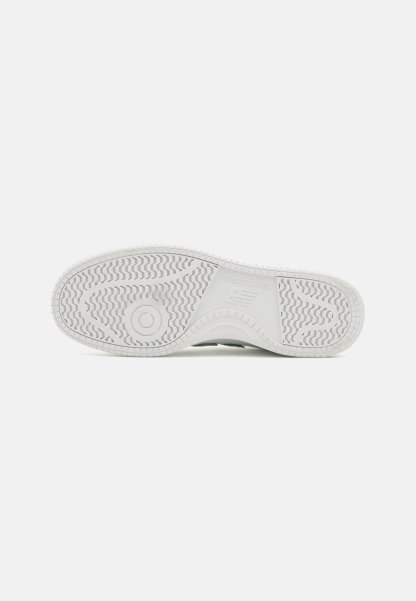 Suela de zapatilla de goma blanca con patrones de textura, que presenta un emblema circular y una sutil marca en la entresuela.