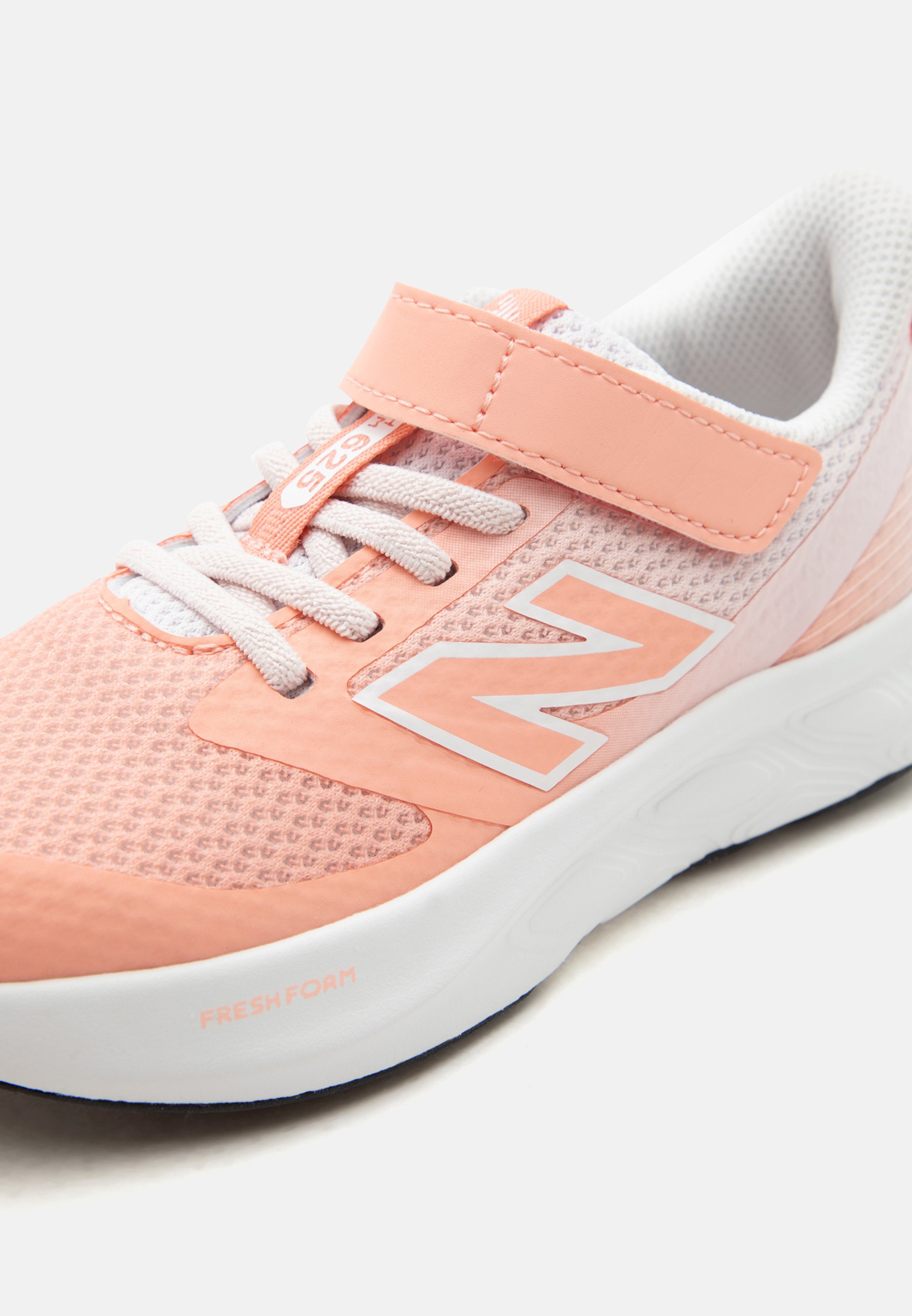 Zapatilla deportiva de color rosa claro y blanco con tejido de malla, cordones blancos, tira de velcro, suela acolchada y logo de la marca en el lateral.