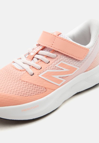 Zapatilla deportiva de color rosa claro y blanco con tejido de malla, cordones blancos, tira de velcro, suela acolchada y logo de la marca en el lateral.