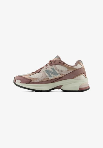 Vista lateral de una zapatilla New Balance rosa y beige con paneles de malla y cuero y una suela blanca gruesa.