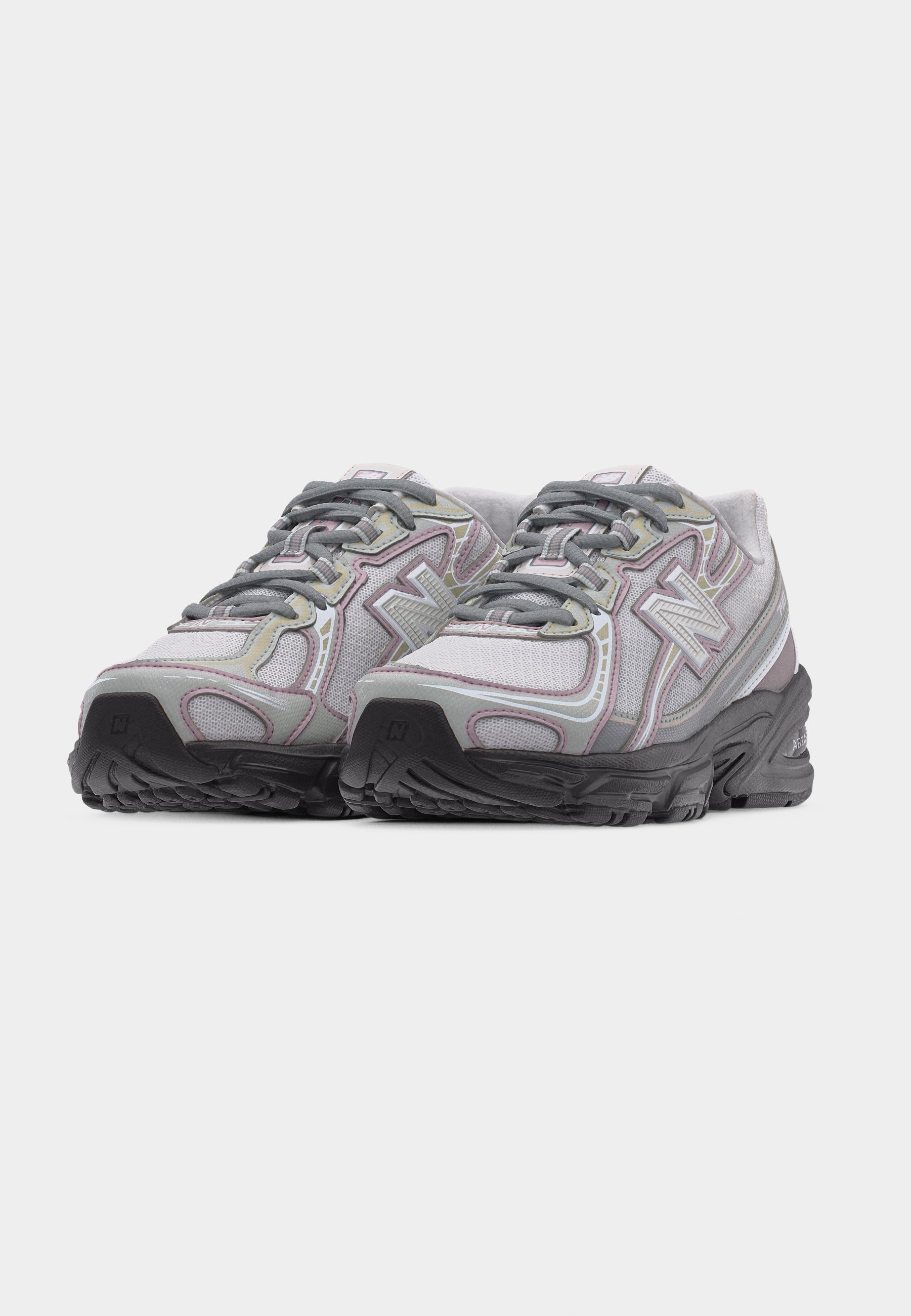 Par de zapatillas deportivas grises y blancas con suelas y cordones negros, que cuentan con superposiciones de malla y sintéticas para soporte y transpirabilidad.
