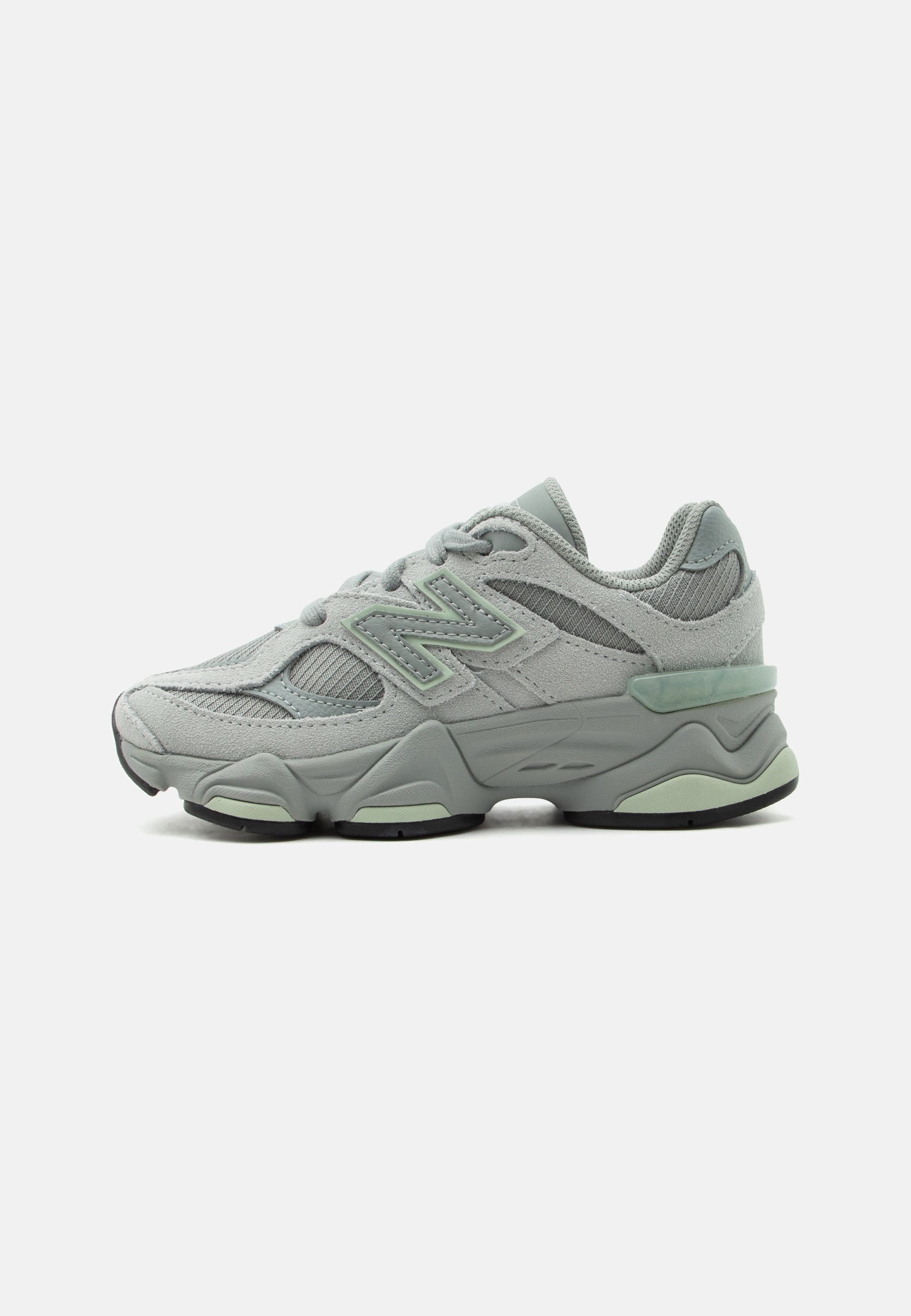 Zapatilla deportiva gris claro con paneles de malla y ante, suela gruesa acolchada, diseño con cordones y detalles de logo lateral.