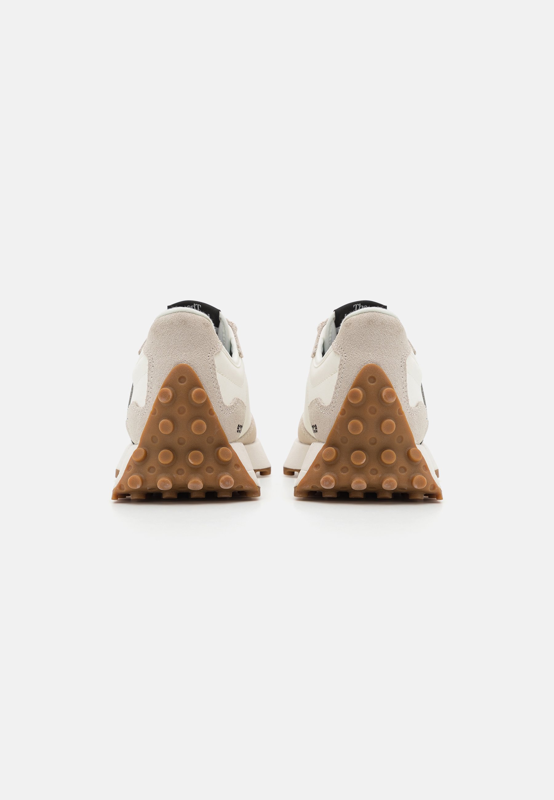 Par de zapatillas beige claras vistas desde atrás, con suelas de tacón triangulares marrones texturizadas con agarres circulares sobre un fondo blanco.