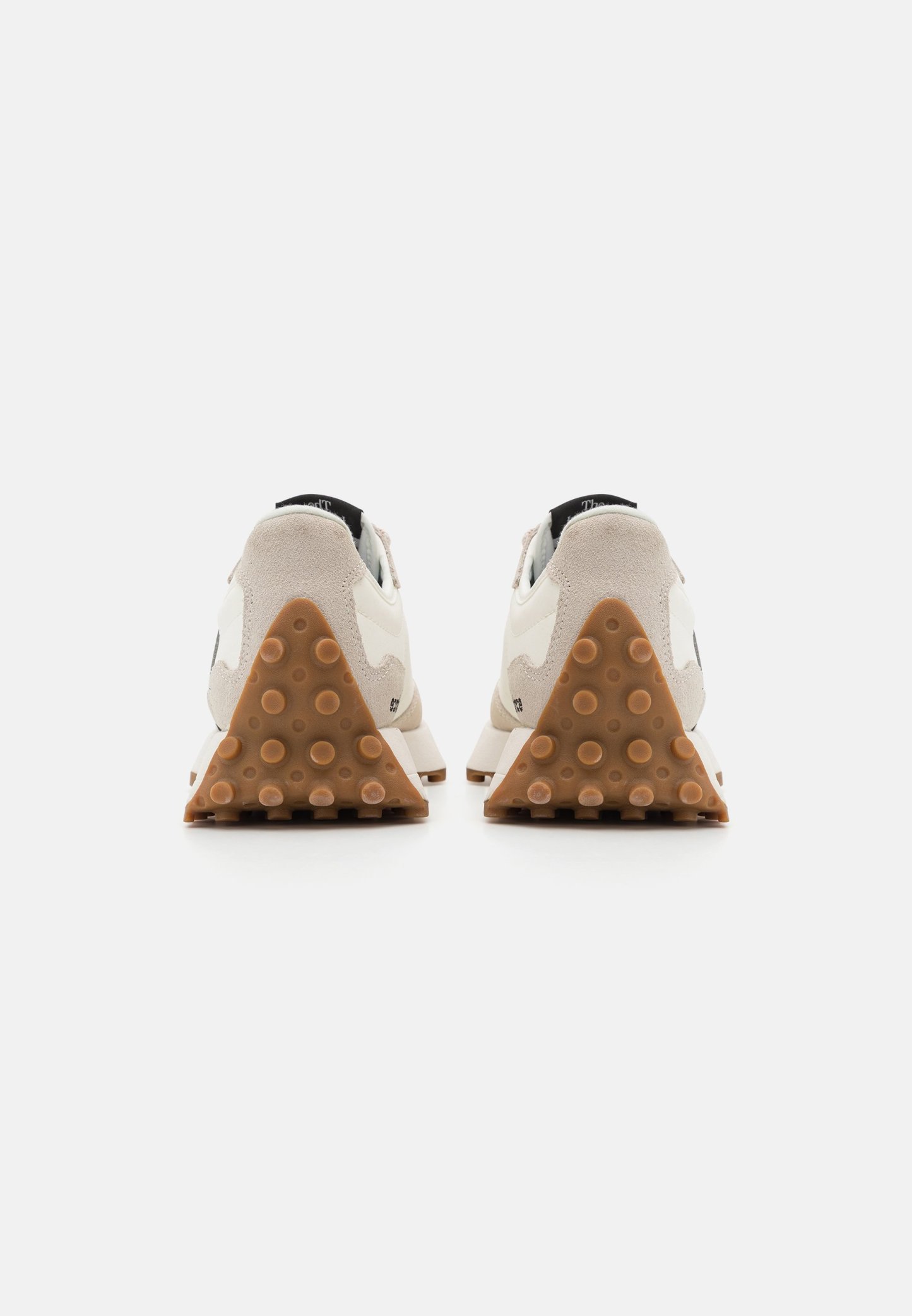 Par de zapatillas beige claras vistas desde atrás, con suelas de tacón triangulares marrones texturizadas con agarres circulares sobre un fondo blanco.