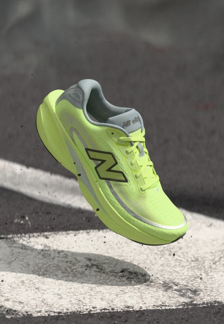 Zapatilla de correr New Balance de color amarillo brillante en el aire sobre asfalto con marcas blancas pintadas en la carretera, mostrando el logotipo en el lateral.