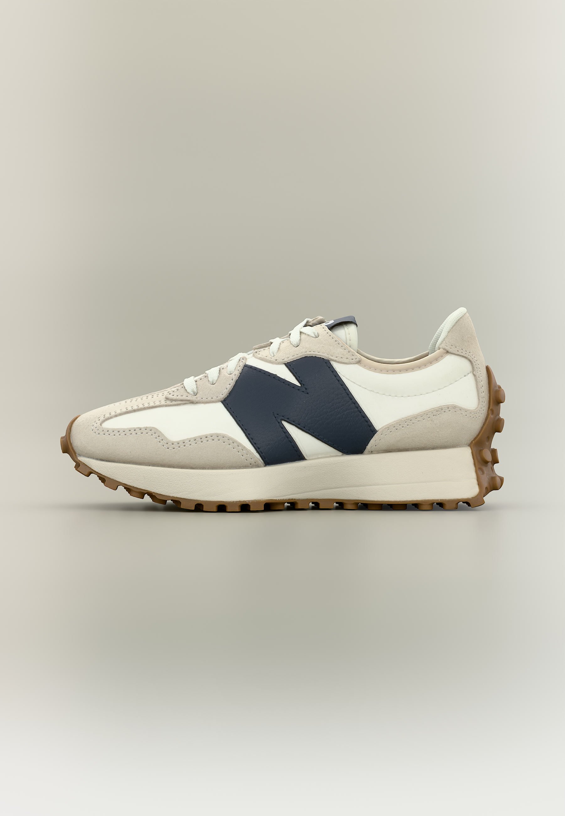 Zapatilla de perfil bajo en beige y blanco con gran logo negro "N", cordones blancos y suela de goma marrón texturizada.