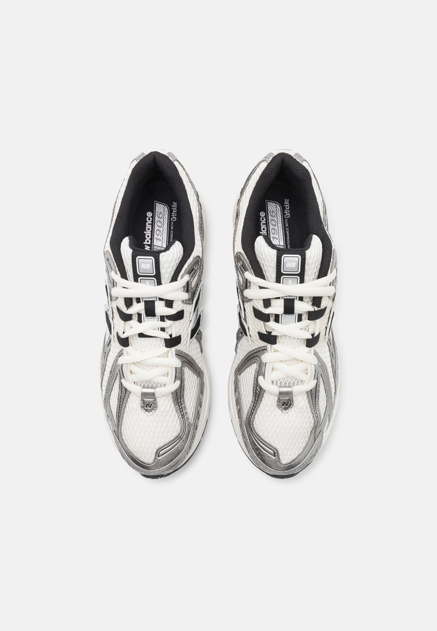 Zapatillas deportivas blancas y grises con parte superior de malla, acentos negros, cordones planos y un collar acolchado para mayor comodidad. Presentan una suela texturizada.