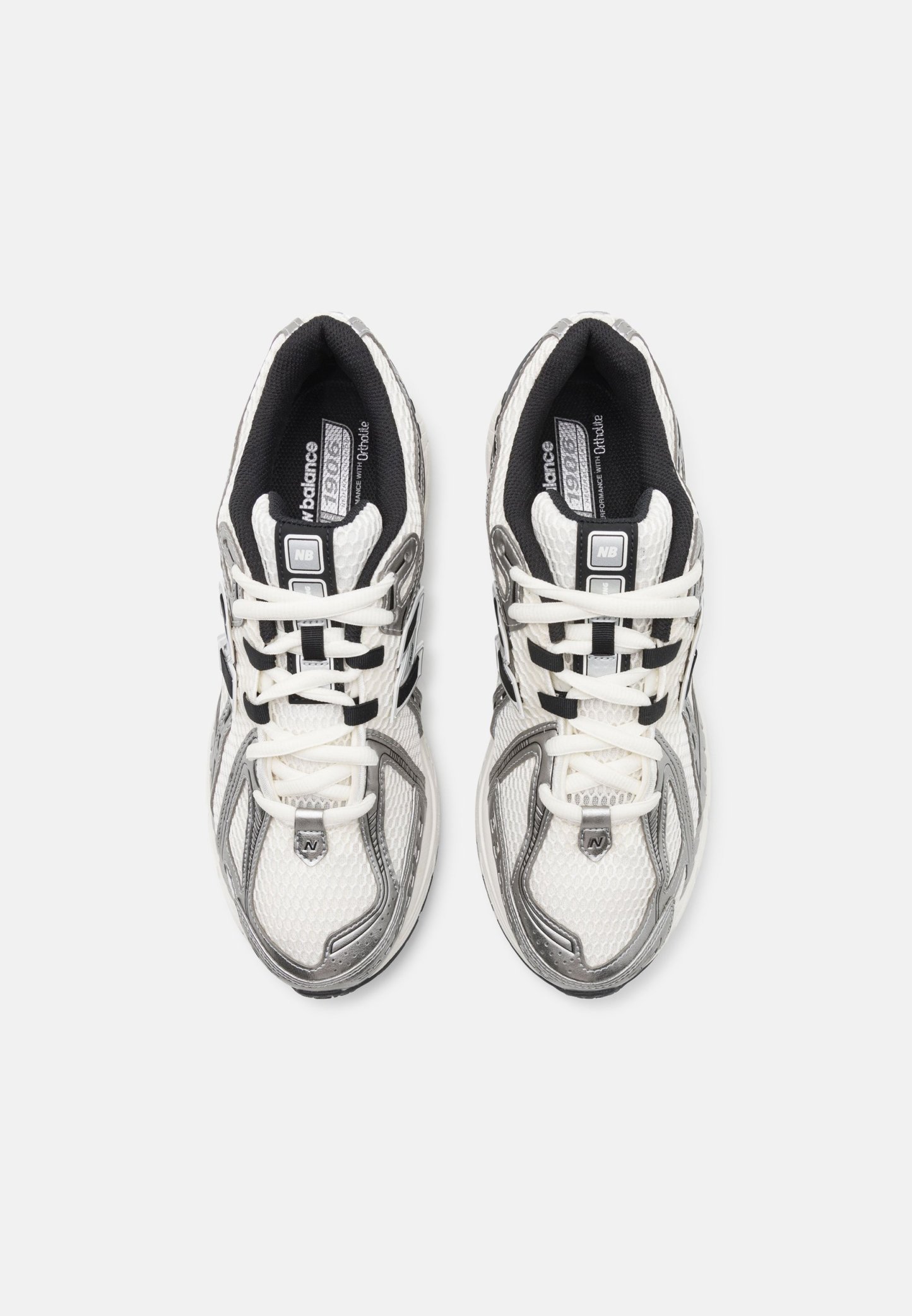Zapatillas deportivas blancas y grises con parte superior de malla, acentos negros, cordones planos y un collar acolchado para mayor comodidad. Presentan una suela texturizada.