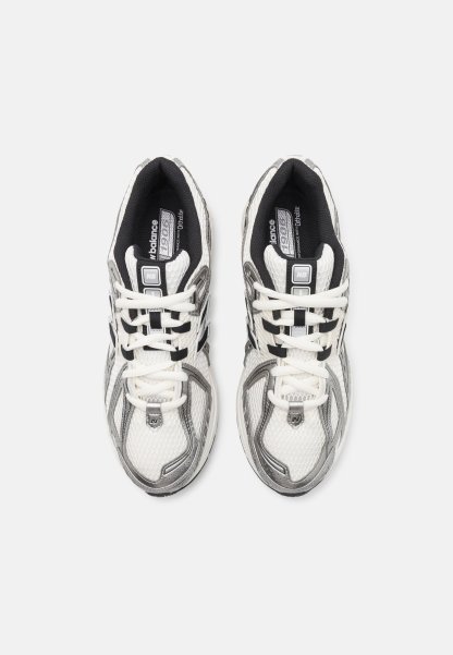 Zapatillas deportivas blancas y grises con parte superior de malla, acentos negros, cordones planos y un collar acolchado para mayor comodidad. Presentan una suela texturizada.