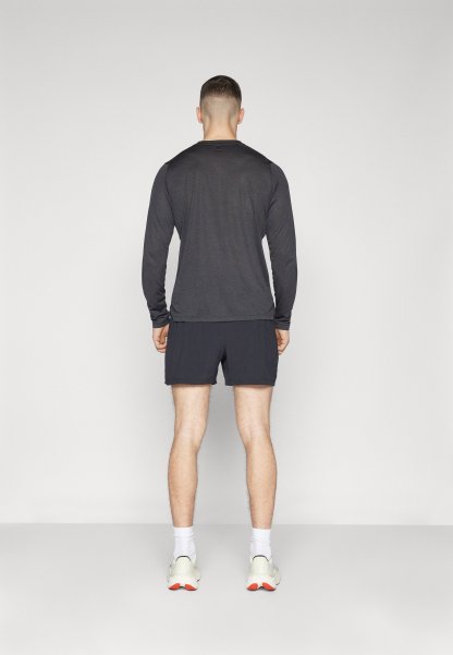 Camisa de manga larga gris combinada con pantalones cortos negros; vista desde la parte de atrás, con un diseño minimalista y un ajuste atlético. Zapatillas blancas visibles.