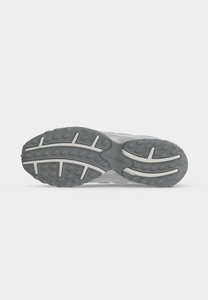 Suela de zapatilla gris y blanca con banda de rodadura de goma texturizada y logo de "New Balance" en el centro sobre un fondo claro y liso.
