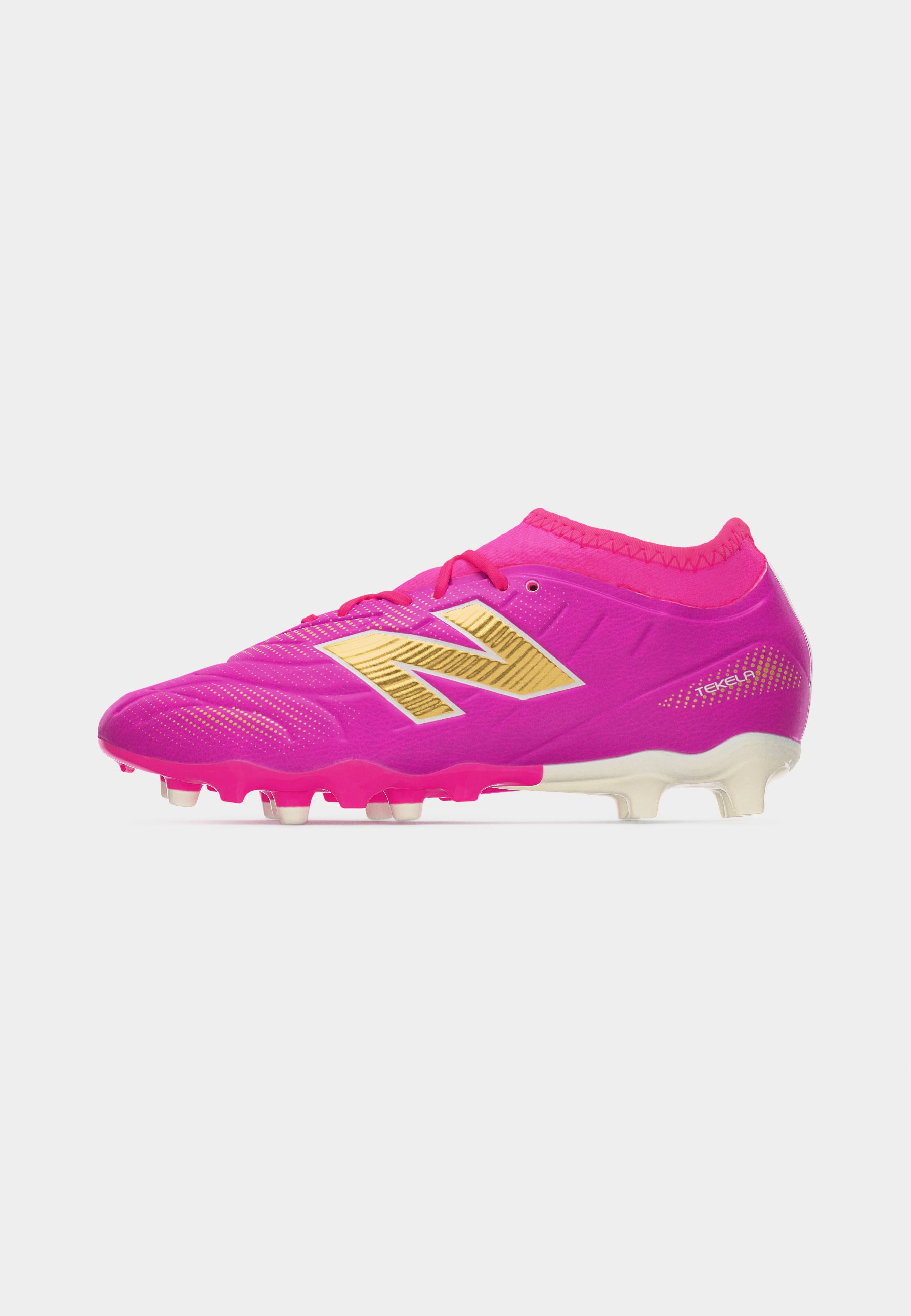 Botín de fútbol de color rosa brillante con logo "N" dorado, diseño de corte bajo y tacos moldeados en suela blanca para juego en terreno firme.