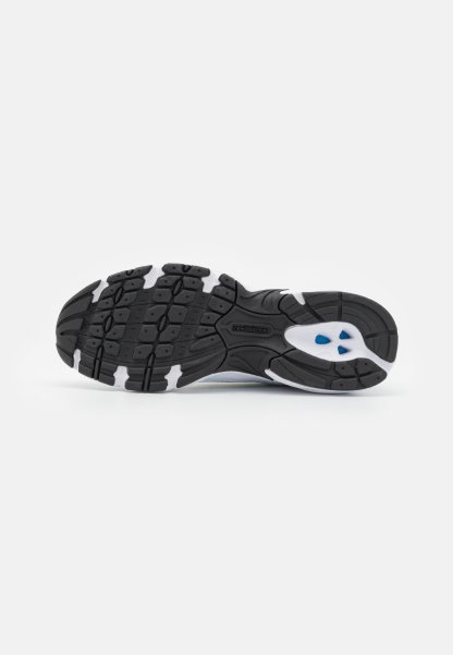 Suela de zapatilla en blanco y negro con patrones de tracción de goma texturizada. Cuenta con pequeños acentos azules y un detalle de logo en el centro.