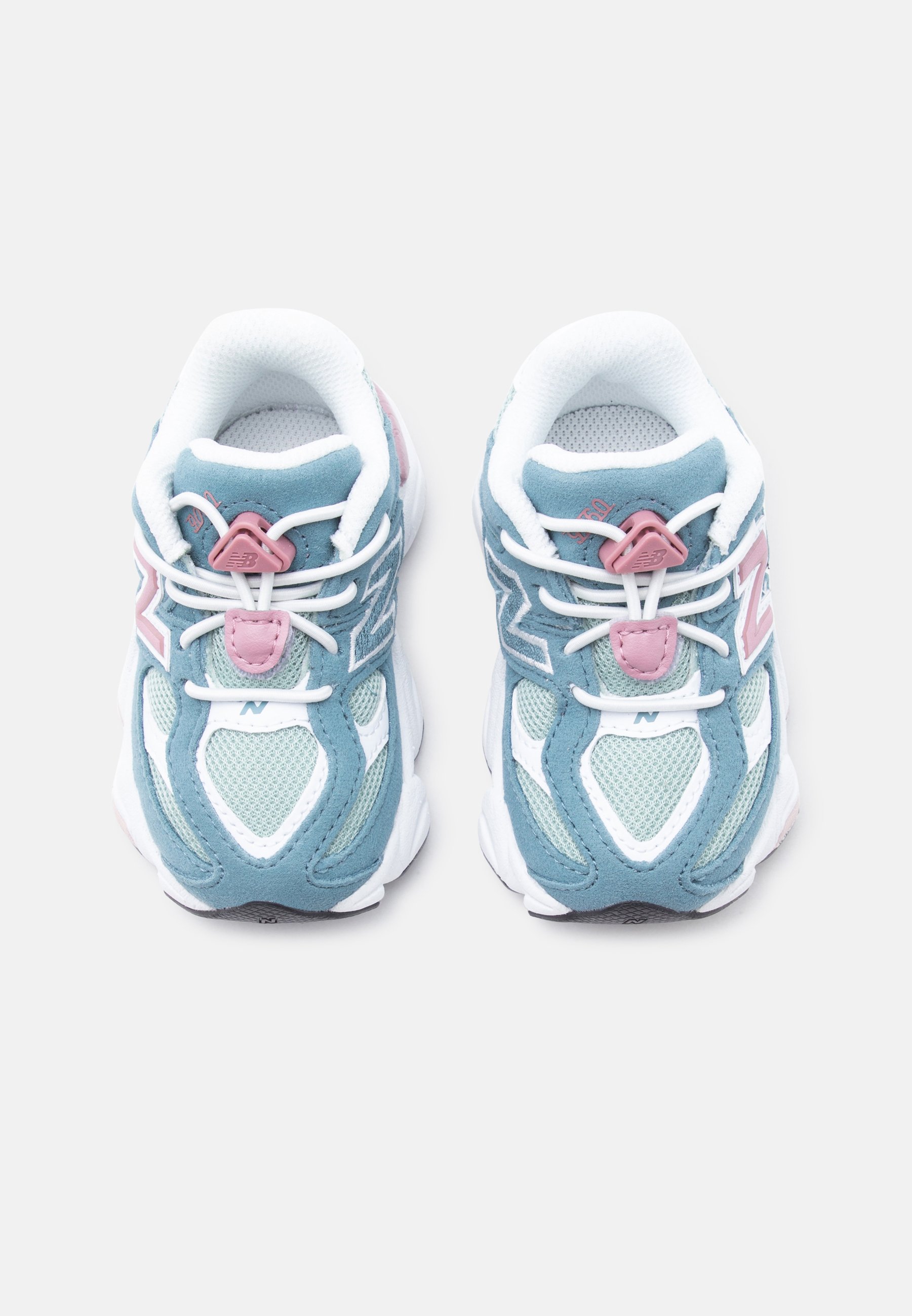 Par de zapatillas azules y blancas con detalles en rosa y cordones elásticos blancos sin atar, vistos desde arriba sobre un fondo liso.