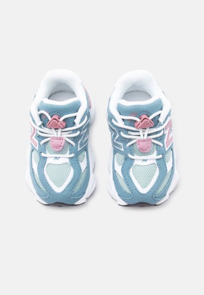 Par de zapatillas azules y blancas con detalles en rosa y cordones elásticos blancos sin atar, vistos desde arriba sobre un fondo liso.
