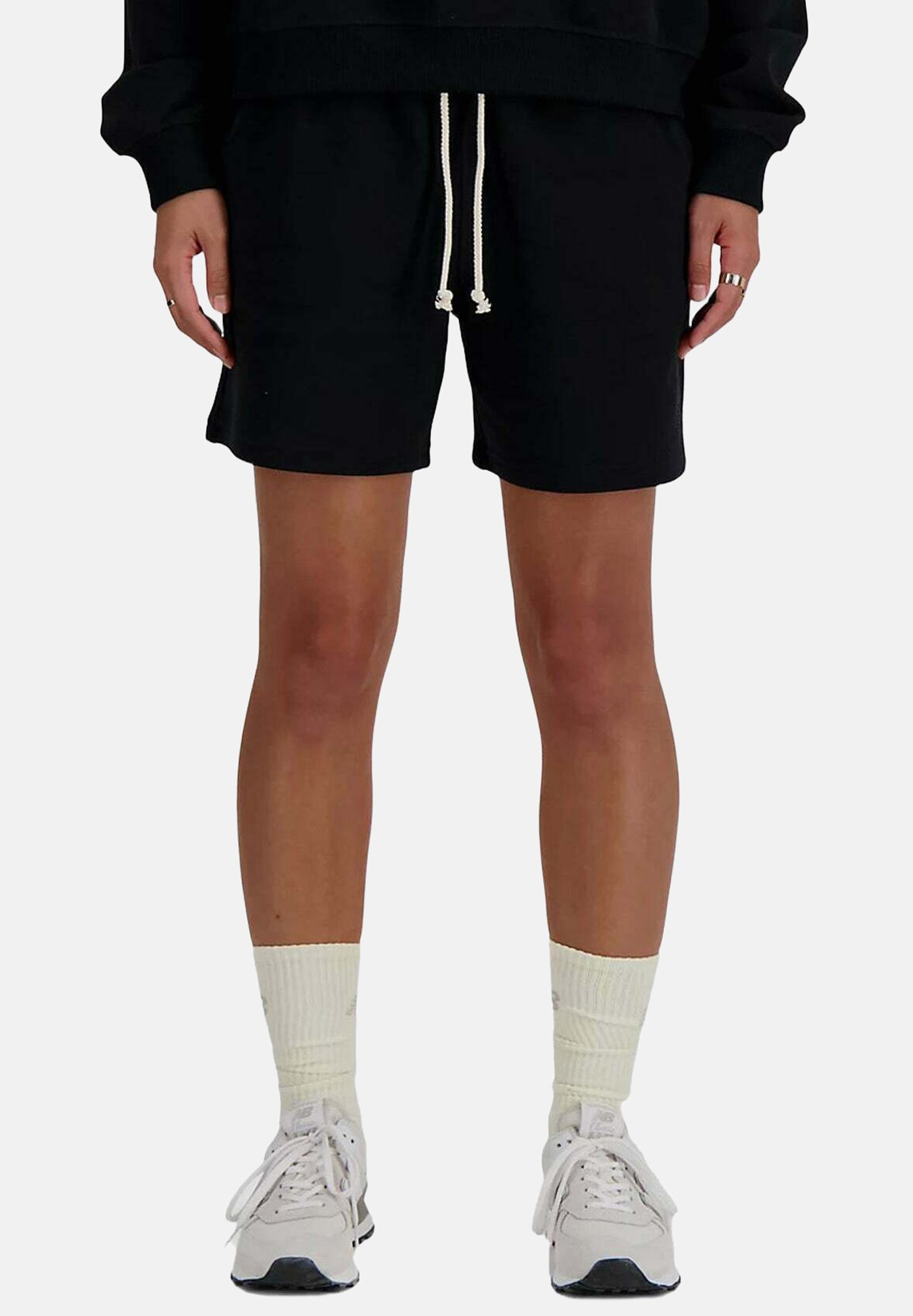 Persona con pantalones cortos negros con cordón, calcetines deportivos blancos y zapatillas blancas, de pie con las manos relajadas a los lados.