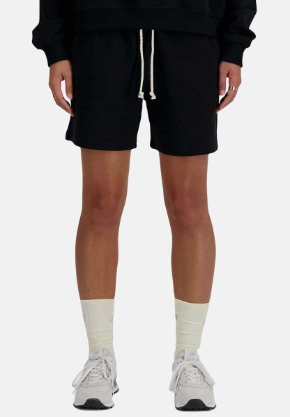 Persona con pantalones cortos negros con cordón, calcetines deportivos blancos y zapatillas blancas, de pie con las manos relajadas a los lados.