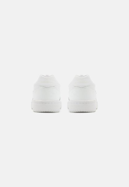 Zapatillas blancas con parte superior de cuero suave, talón acolchado y suela de goma texturizada. Presenta un logotipo sutil en el talón. Diseño minimalista.