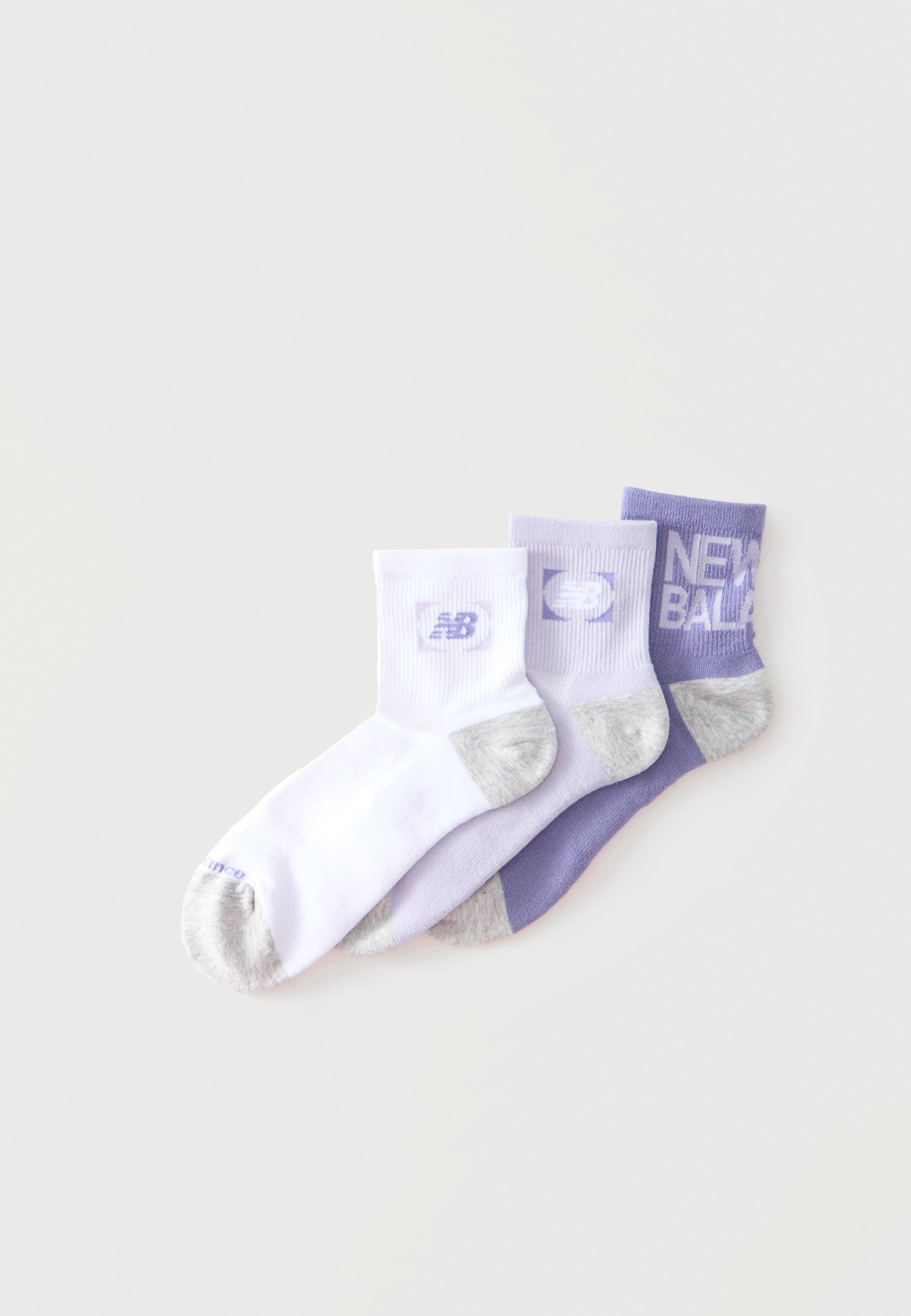 Tres pares de calcetines tobilleros en blanco y tonos de morado, cada uno con punteras y tacones grises y logos de New Balance en los puños.