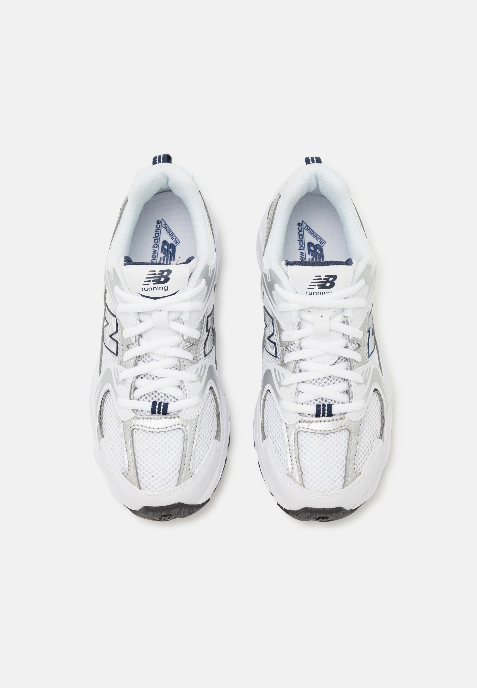 Zapatillas deportivas blancas con parte superior de malla y sintético, con una suela gris, acentos en azul marino y cordones en contraste. Se pueden ver dos logotipos de "N".