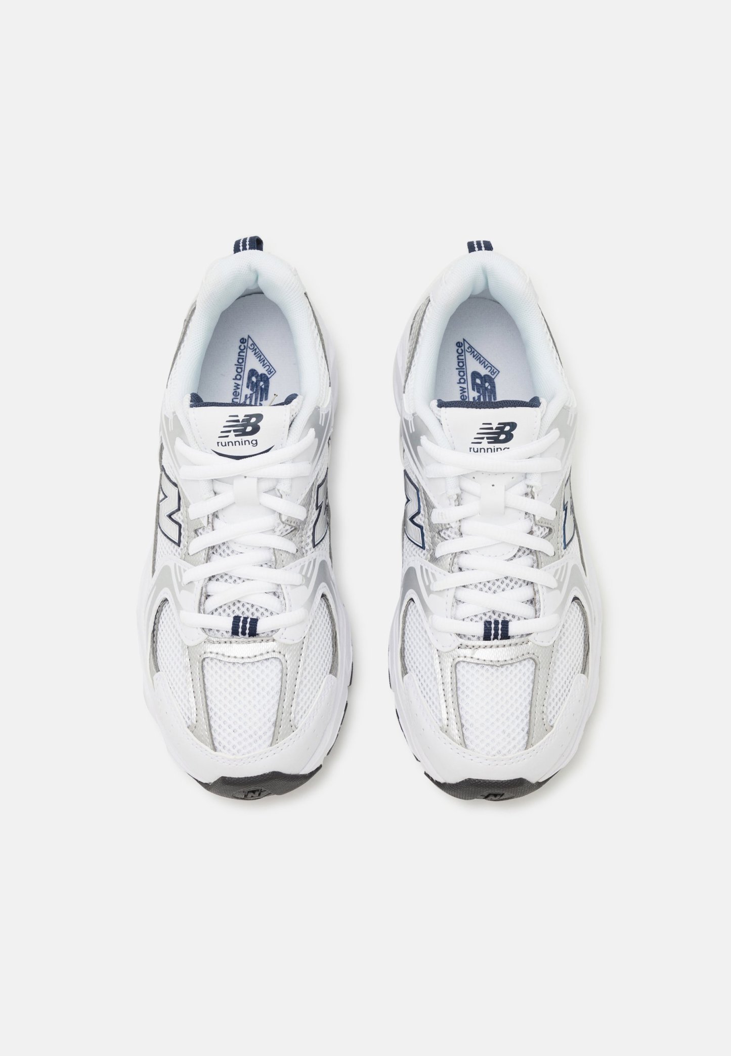 Zapatillas deportivas blancas con parte superior de malla y sintético, con una suela gris, acentos en azul marino y cordones en contraste. Se pueden ver dos logotipos de "N".