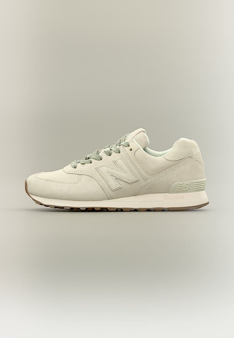 Zapatilla beige de New Balance con textura de ante, diseño con cordones y suela de goma, mostrada de lado sobre un fondo neutro.