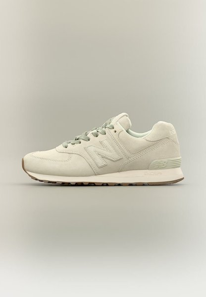 Zapatilla beige de New Balance con textura de ante, diseño con cordones y suela de goma, mostrada de lado sobre un fondo neutro.