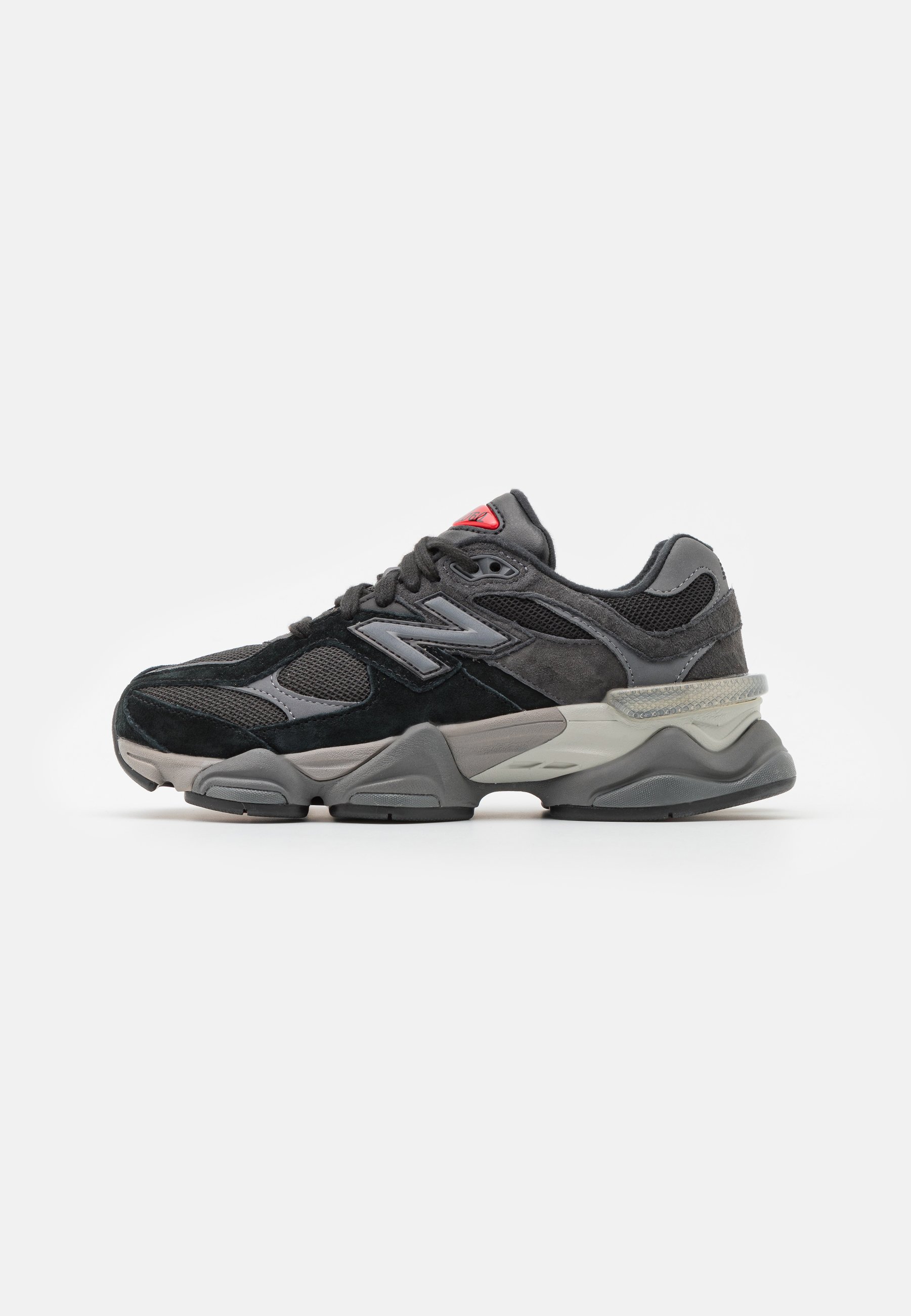 Zapatilla negra y gris con una mezcla de materiales de ante y malla, suela gruesa, logotipo prominente y acento rojo en la lengüeta.
