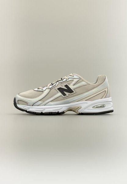 Zapatilla de running New Balance beige y blanca con logo negro, suela acolchada etiquetada como ABZORB y cordones beige sobre un fondo neutro.