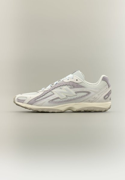 Zapatilla New Balance blanca y gris claro con parte superior de malla y ante, suela acolchada y diseño con cordones, mostrada de perfil.