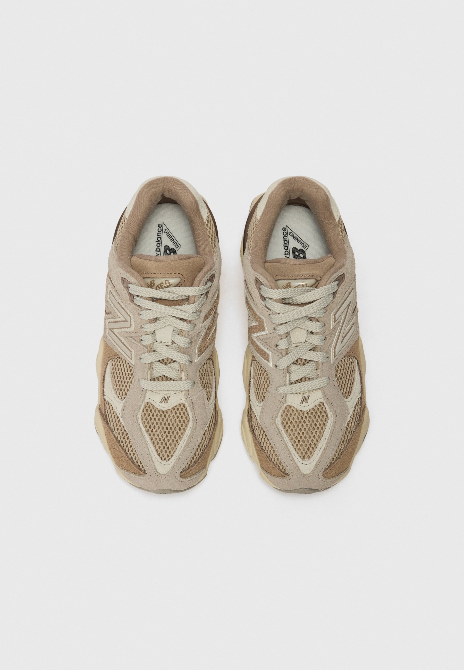 Zapatillas deportivas beige que combinan materiales de malla y ante, con cordones y una suela voluminosa. Superficies texturizadas añaden elementos de diseño estructural.