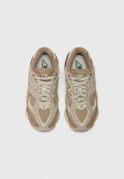 Zapatillas deportivas beige que combinan materiales de malla y ante, con cordones y una suela voluminosa. Superficies texturizadas añaden elementos de diseño estructural.