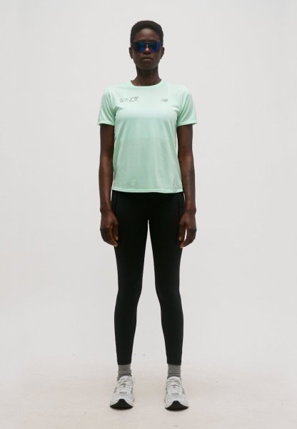 Persona vistiendo una camiseta deportiva de manga corta color verde menta, leggings negros, calcetines grises, zapatillas blancas y gafas deportivas azul reflectantes, de pie y erguida.