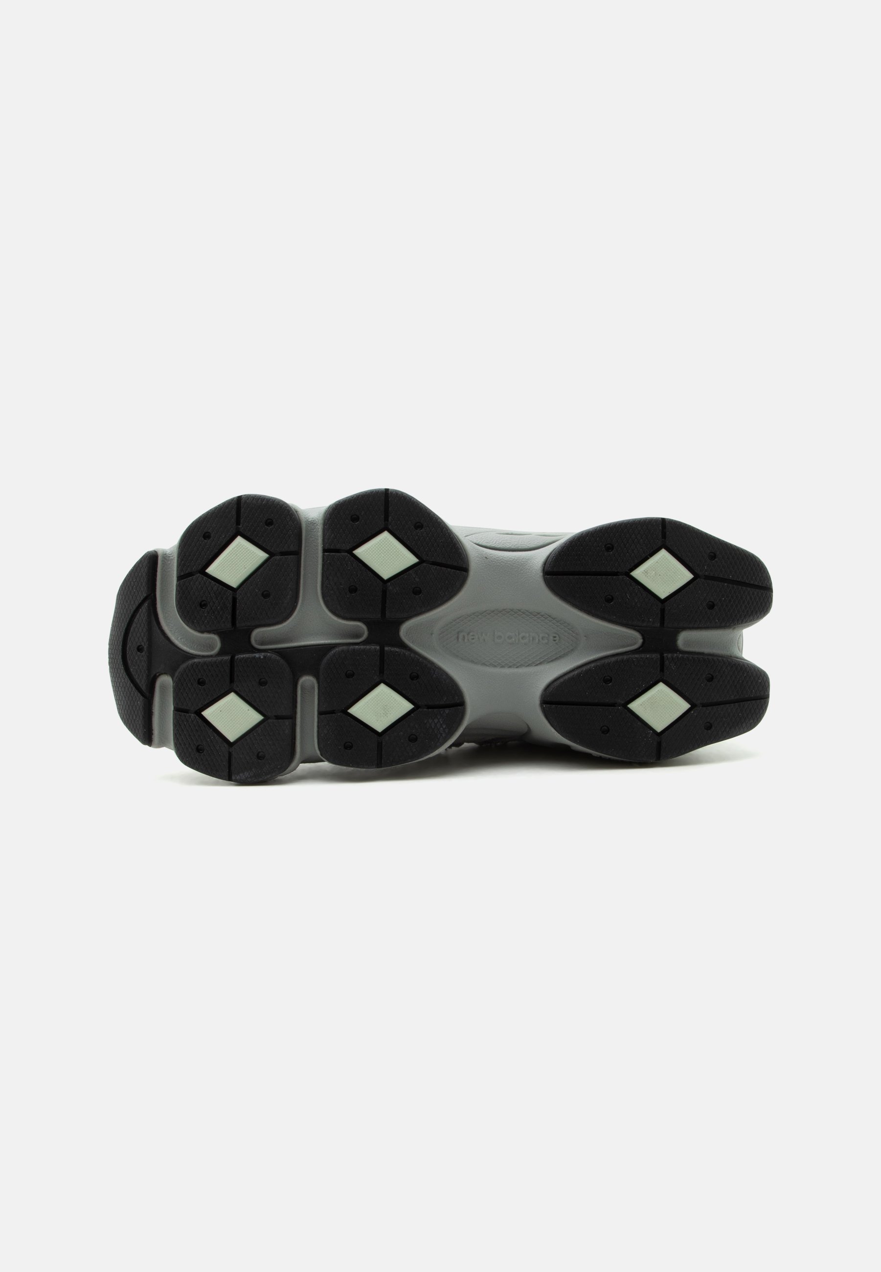 Suela de zapatilla New Balance gris con bandas de goma negras y patrones de tracción en forma de diamante de color verde claro sobre un fondo blanco.