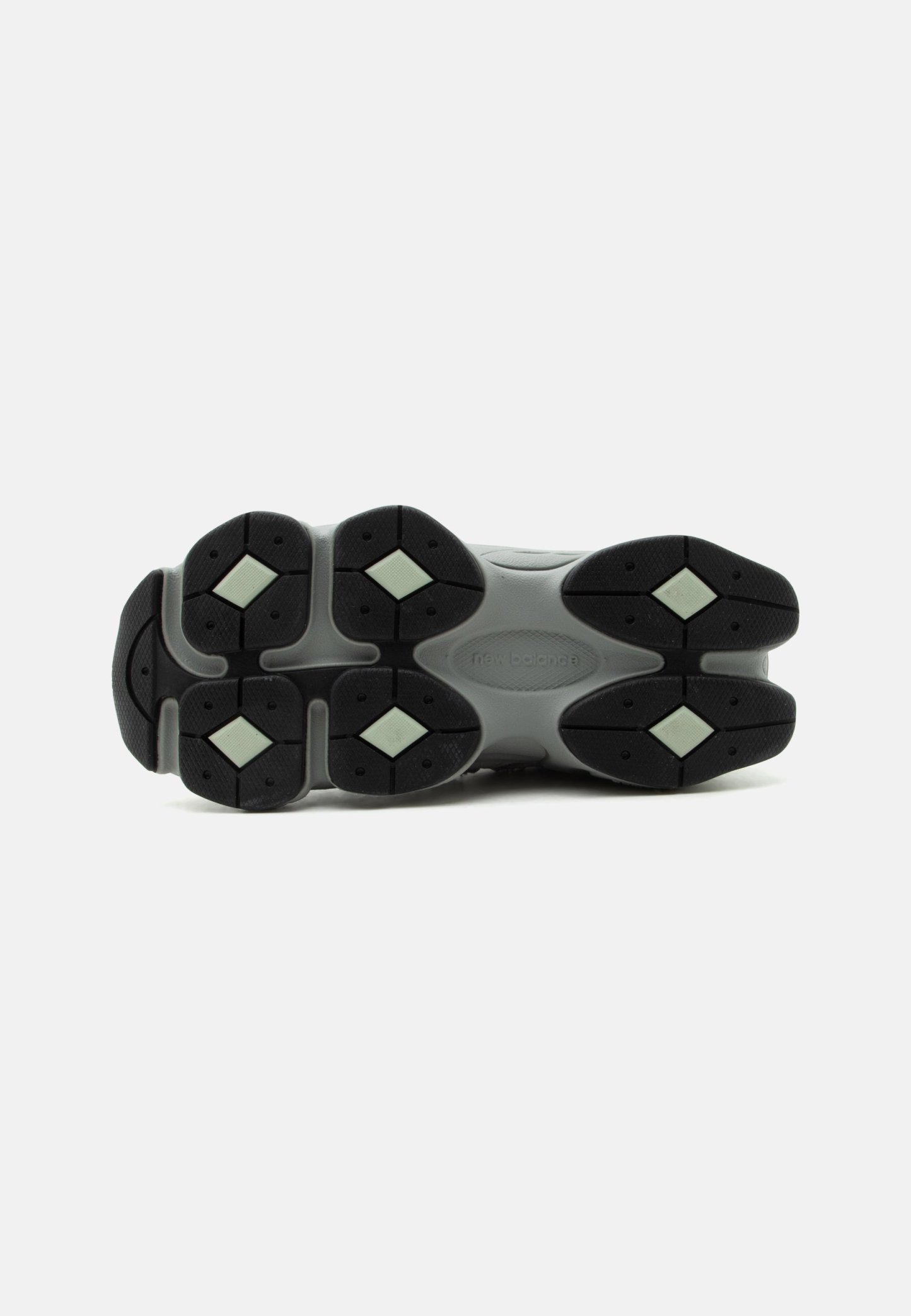 Suela de zapatilla New Balance gris con bandas de goma negras y patrones de tracción en forma de diamante de color verde claro sobre un fondo blanco.