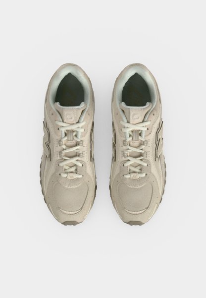 Par de zapatillas deportivas beige con cordones blancos, vistas desde arriba sobre un fondo blanco liso.