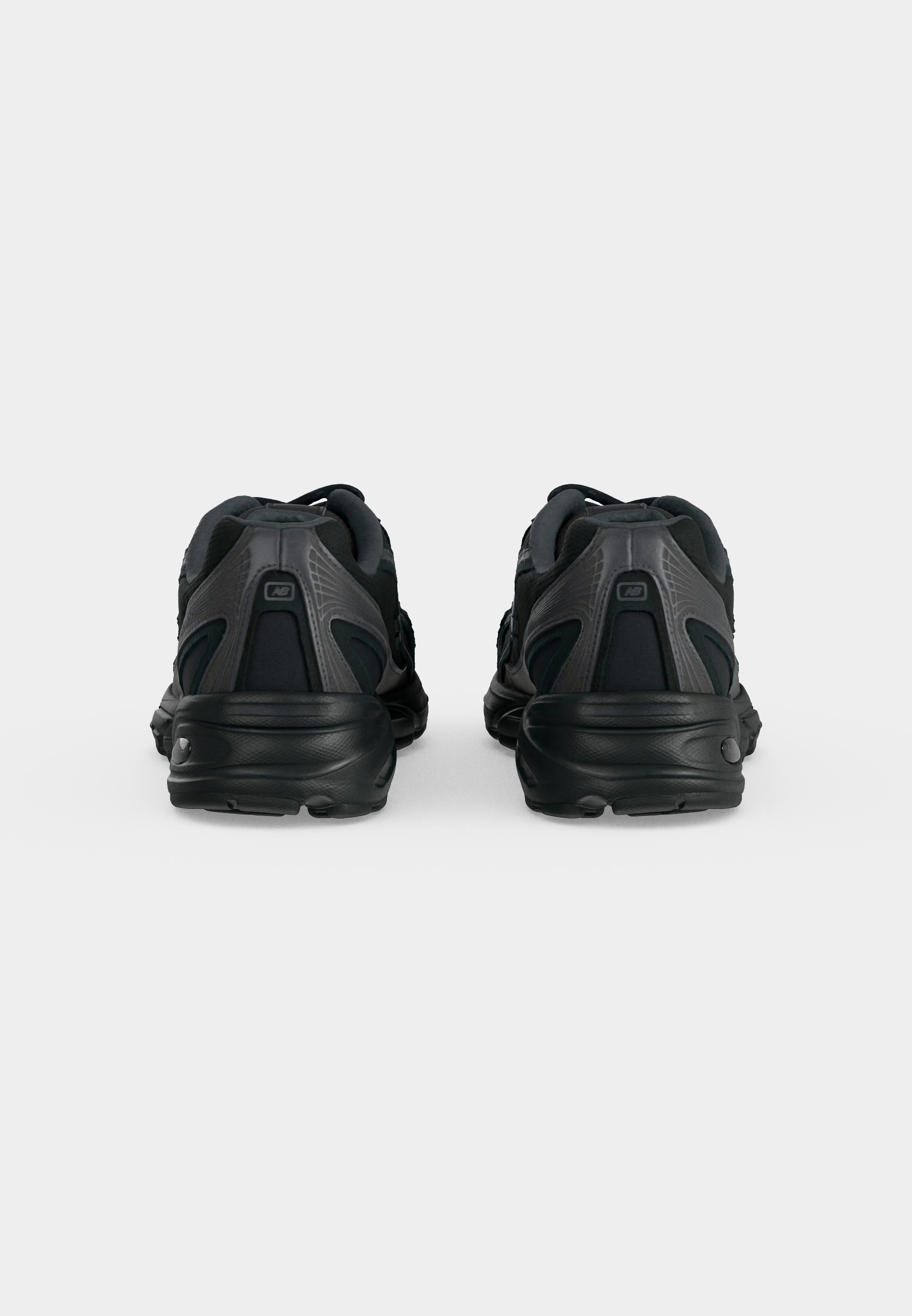 Par de zapatillas deportivas negras vistas desde atrás, con detalles de paneles texturizados y lisos sobre un fondo claro y liso.