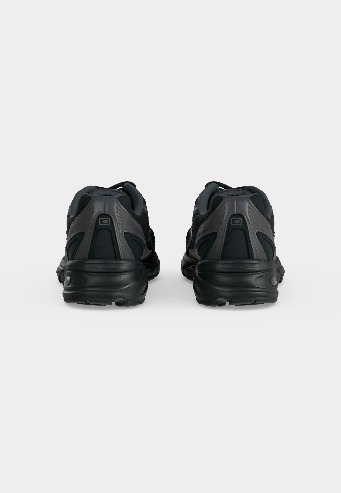 Par de zapatillas deportivas negras vistas desde atrás, con detalles de paneles texturizados y lisos sobre un fondo claro y liso.