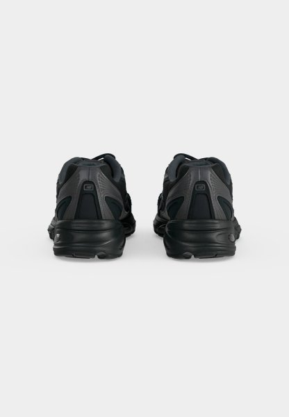 Par de zapatillas deportivas negras vistas desde atrás, con detalles de paneles texturizados y lisos sobre un fondo claro y liso.