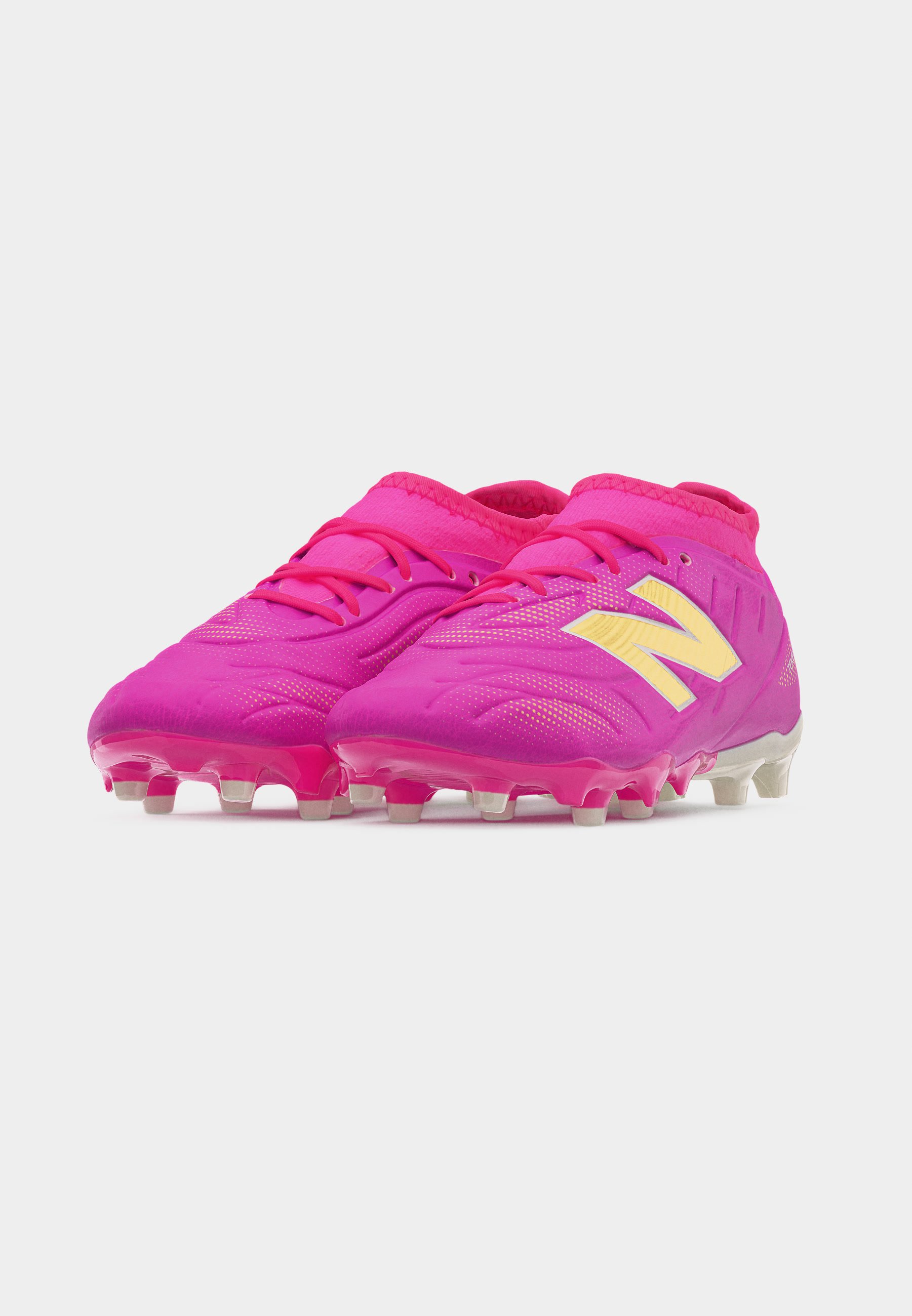 Par de botines de fútbol de color rosa brillante con logotipos amarillos de New Balance y tacos de plástico moldeado sobre fondo blanco.