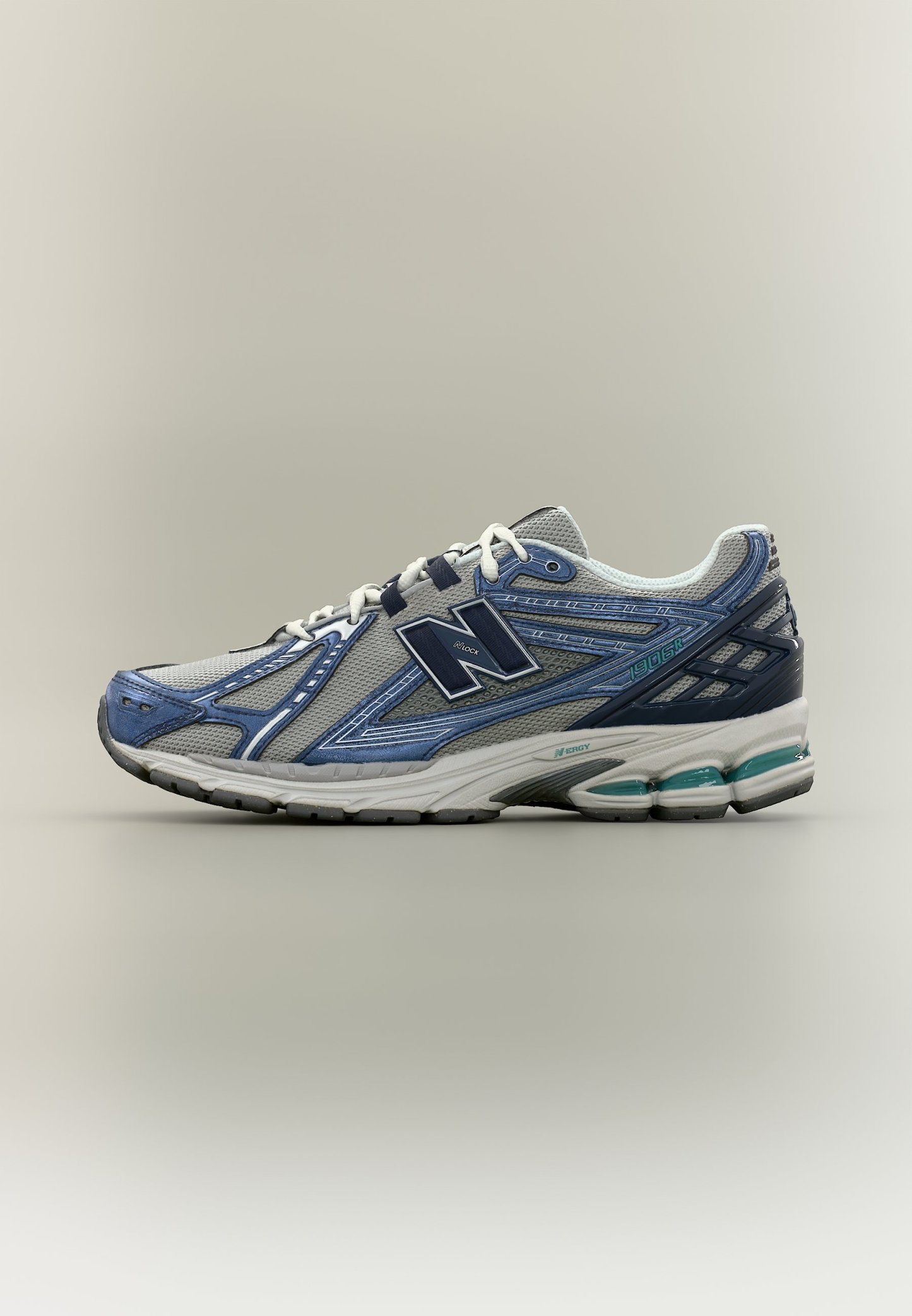 Zapatilla deportiva New Balance en gris y azul con cordones blancos, suela acolchada y parte superior de tela de malla vista de lado sobre fondo neutro.