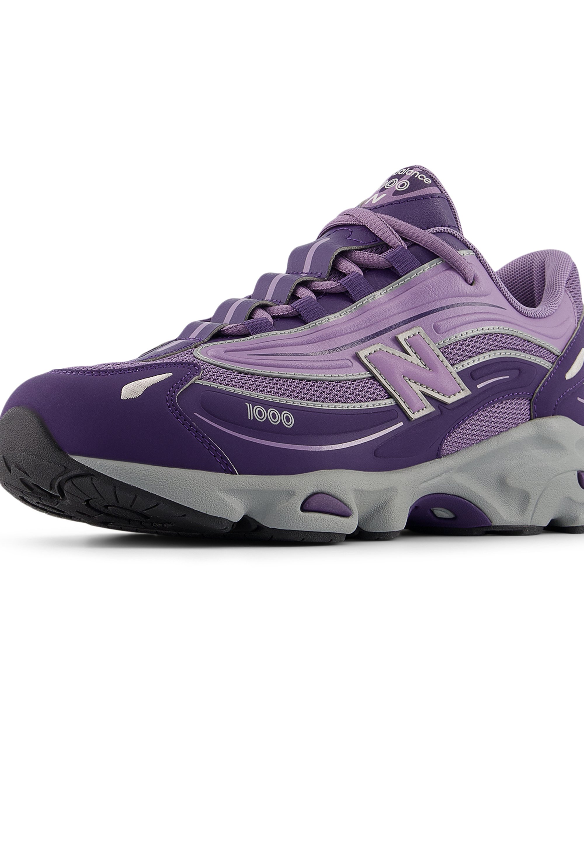 Zapatilla de deporte morada con parte superior de malla y material sintético. Cuenta con suela de goma, diseño con cordones y detalles reflectantes. Modelo 1000 de New Balance.