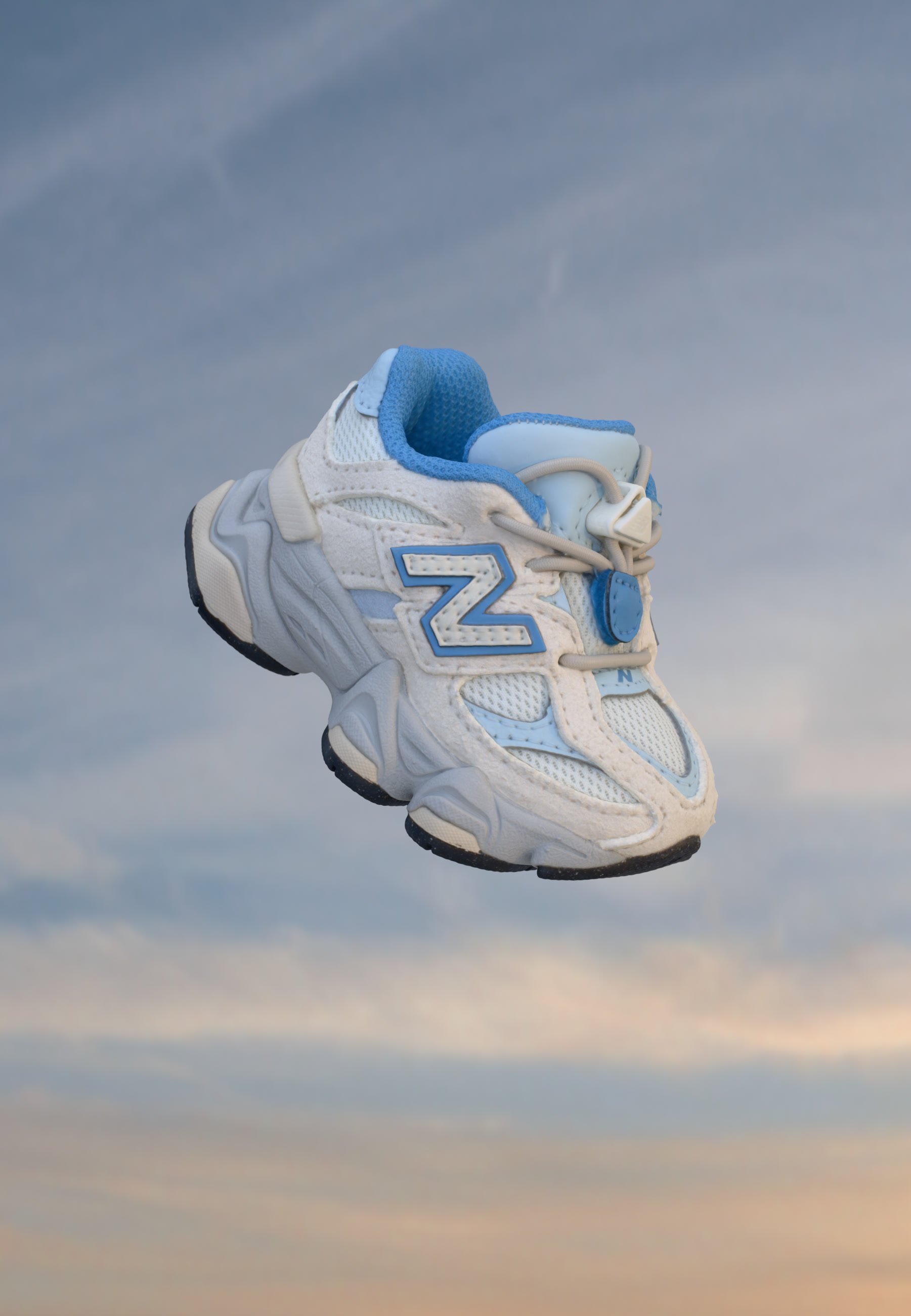Zapatilla deportiva blanca y azul claro con suela gruesa flotando sobre un fondo de cielo nublado.