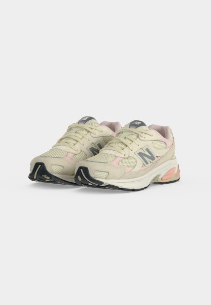 Par de zapatillas de correr New Balance beige y rosa claro con detalles de rejilla y ante, suela exterior negra y logo en los laterales y la lengüeta.