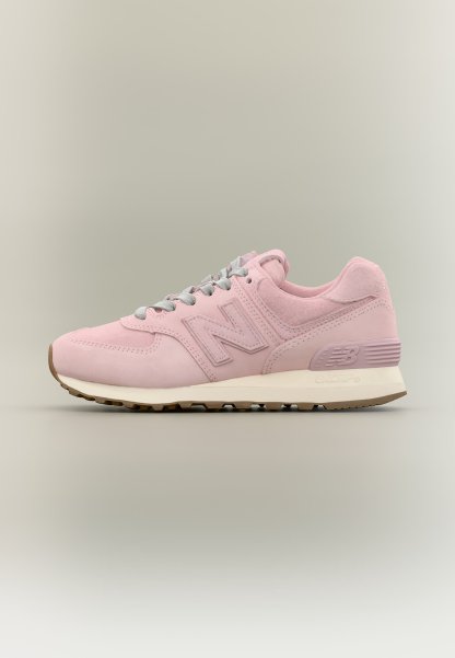 Zapatilla New Balance rosa con cordones grises, entresuela blanca y suela exterior de goma marrón mostrada de perfil sobre fondo neutro.