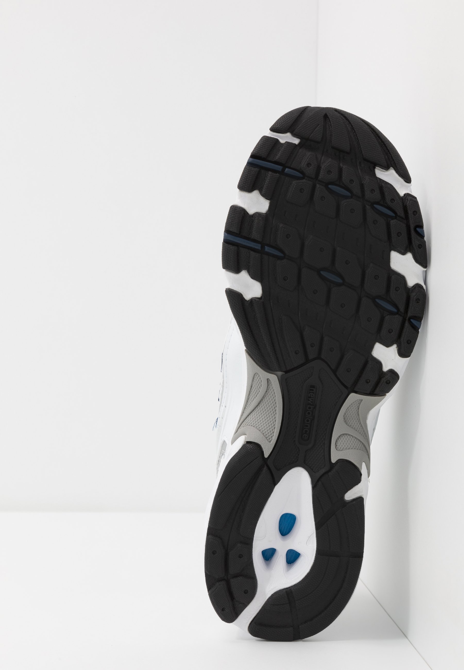 Suela de zapatilla deportiva en blanco y negro con goma texturizada, con un diseño curvado, detalles de acento en azul y un área del talón reforzada.
