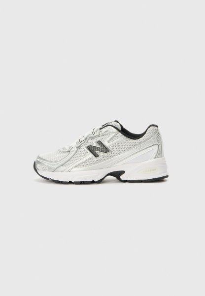 Zapatilla deportiva blanca y gris con empeine de malla, logo negro en el lateral, forro interior negro y suela blanca gruesa con dibujo negro.