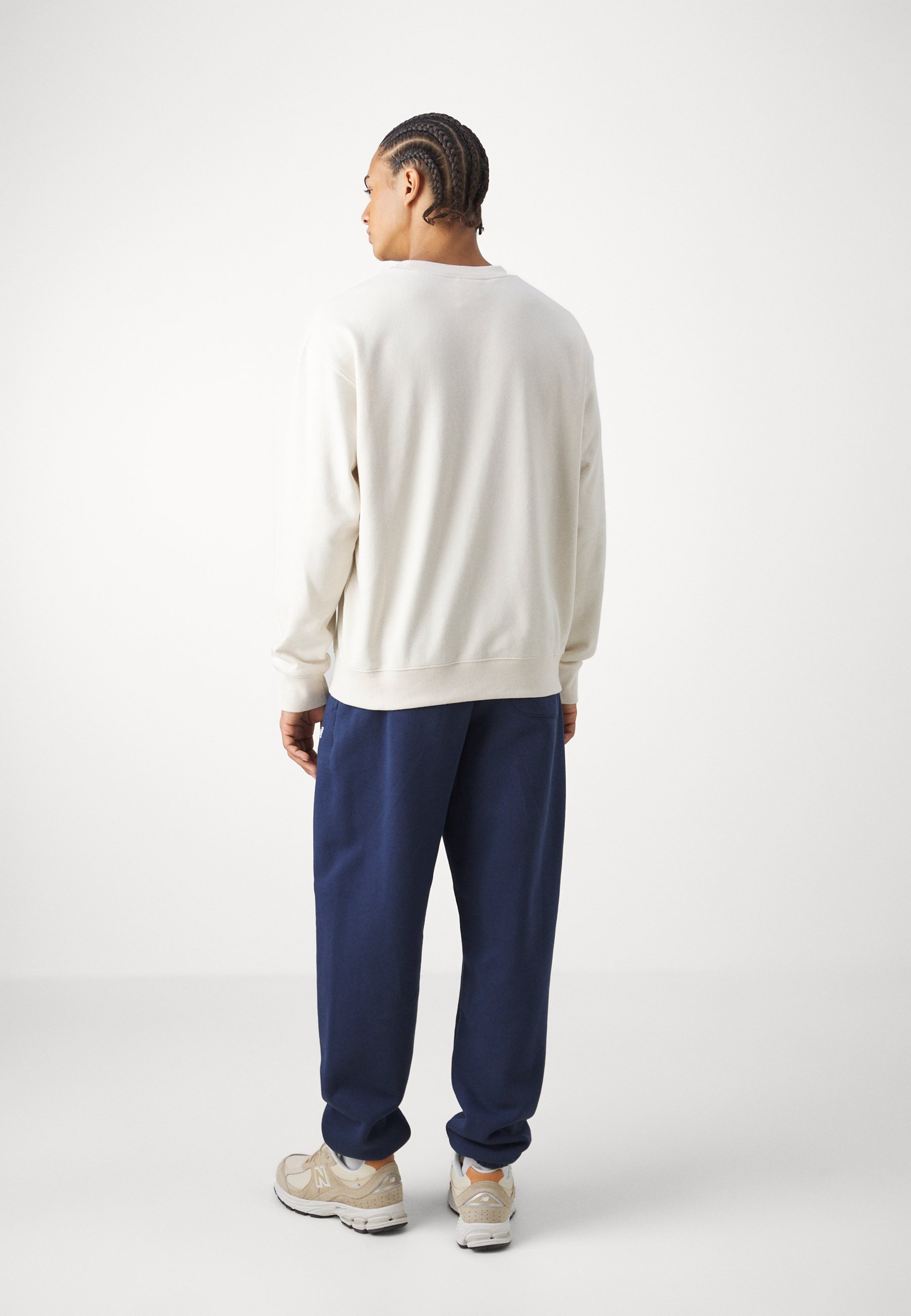 Sudadera crema con cuello redondo y mangas largas, combinada con pantalones azul marino. La tela parece suave, con puños y cinturilla de canalé.