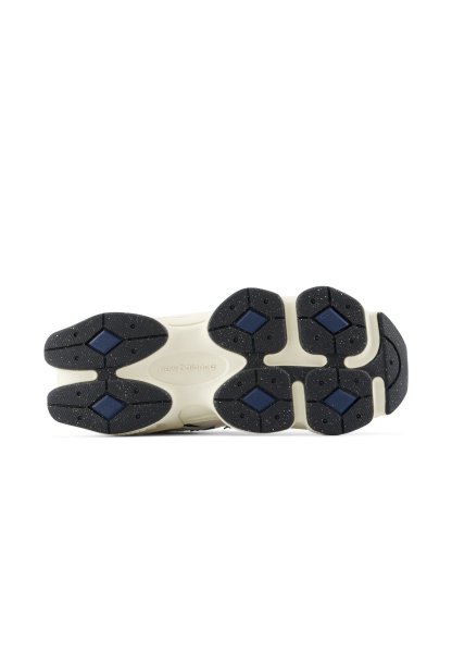 Suela exterior de un zapato New Balance que muestra una suela blanca con seis almohadillas de tracción de goma negra, cada una con una forma de diamante azul en el centro.
